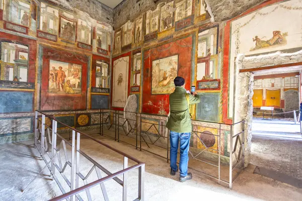 Ziyaretçiler, İtalya 'nın Pompei kentindeki arkeoloji sahasındaki Vettii Hanesi' nin duvarlarında mitolojik sahneler ve günlük yaşamı tasvir eden canlı ve iyi korunmuş fresklere hayranlık duyuyorlar.