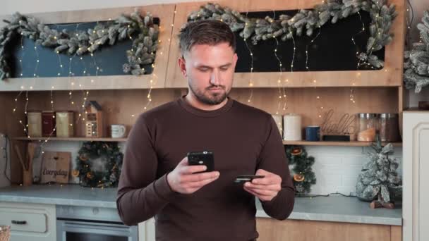 魅力的な幸せな男の夫は 携帯電話のクレジットカードを使用してオンラインで購入し インターネット上で新年の贈り物を購入する最高の価格 クリスマスイブ販売 安全な支払い 電子商取引 電子ショッピング活動を楽しむ — ストック動画