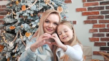 Güzel aile annesi ve kızı kalp şeklini gösterdiler parmaklarını birleştirdiler, video blogcuları sevgilerini paylaştılar aboneleri tebrik ettiler Mutlu Noeller. Yeni yıl kutlaması, mutlu kış tatilleri, en iyi dilekler konsepti
