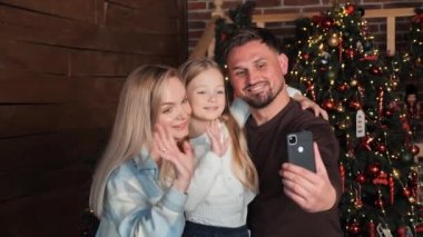 Güzel evli bir çift ve çocukları akıllı telefon kullanarak arkadaşlarıyla konuşuyorlardı. Video konferans uygulaması ile Mutlu Noeller diliyor. Modern teknoloji yeni yıl 2023 tebrikler. Tatil kutlamaları