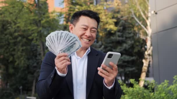 Azjatycki Szczęśliwy Biznesmen Garniturze Telefonem Komórkowym Machając Pieniądze Świętować Zwycięstwo — Wideo stockowe