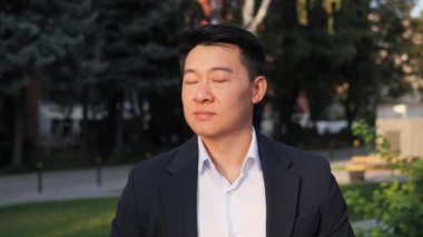 Kameraya bakan başarılı, gülümseyen Asyalı genç bir iş adamının portresi. Dışarıda poz veren şık giyinen mutlu bir iş adamı. Başarılı erkek profesyonel lider.