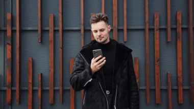 Başarılı bir iş adamı, elinde Smartphone Walking ile kalın sonbahar giysileri giyiyor. Dışarıdaki Mobil Aygıt Daktilo mesajını kullanan mutlu adam. Smartphone Screen 'e bakıyor ve gülümsüyor. Yeni Mobil Uygulama