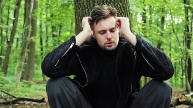Üzgün erkek yüzünü kapat. Üzgün, stresli bir adam. Ağacın altında oturuyor, kafasını tutuyor. Derin depresyon yüzünden ağlıyor.