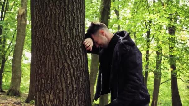 深いうつ病のために泣いて 彼の頭を保持する森の中の木の近くに立っている悲しいストレスの男性の顔を動揺顔の表情トラブルの問題を心配 — ストック動画