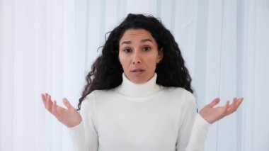 Kafası karışmış Latin kadının portresi beyaz arka planda omuz silkiyor. Yakından bakınca gerçek bir kız tabela gösteriyor. Bilmiyorum, yardımcı olamıyorum. Kıvırcık saçlı, güzel model. Soru yok.