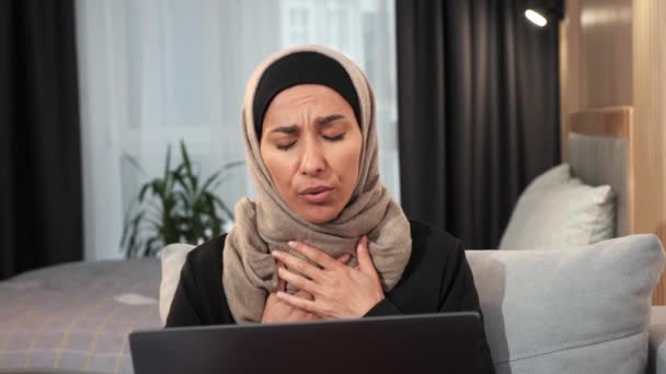 头戴头巾的心烦意乱的穆斯林悲伤女孩独自坐在家里 一边工作一边恐慌发作 感觉很糟糕 沮丧的穆斯林妇女患有疾病 呼吸有问题 需要帮助的医生 — 图库视频影像