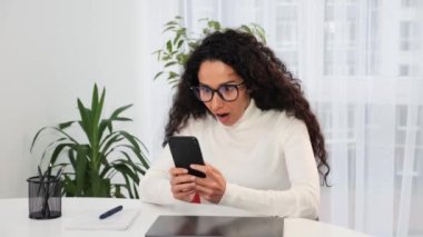 Neşeli Latin kadın evde online zaferini kutluyor, cep telefonu kontrol e-posta uygulaması kullanıyor piyango kazanınca mutlu görünüyor. Kazanan başarı anının tadını çıkarır, bahis konsepti.