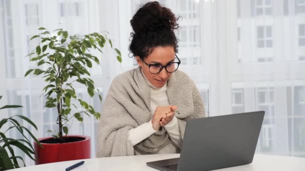 一个裹着格子花的西班牙女孩正在一台笔记本电脑上工作 这名妇女因缺乏暖气 不工作的空调而冻僵 并因感冒而病倒 生病的年轻女商人在家里洗手 — 图库视频影像