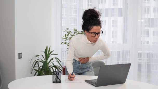 自宅でラップトップで働く若い女性のフリーランスは 突然の月経腹部痛胃炎不快感下痢肝問題虫垂炎症状消化不良胃痙攣痛室内 — ストック動画