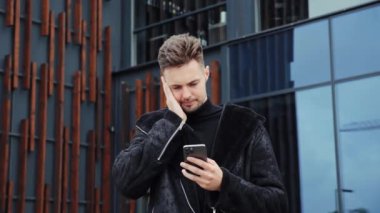 Şehir arka planında cep telefonundan kötü haber okuyan sinirli adamın portresi. Şehir caddesinde sinirli bir adam akıllı telefon ekranına bakıyor. Sinirli adam cep telefonundan mesaj üstüne öfke hissediyor.