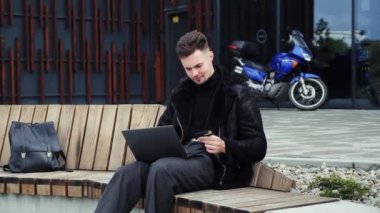 Moda işadamı dışarıda bankta otururken dizüstü bilgisayarından ödeme yapıyor. İnternet sitesinde kredi kartı numarası yazan genç ve çekici bir adam. İnternetten alışveriş konsepti. Parayı geri çek. Ödeme aktarımı