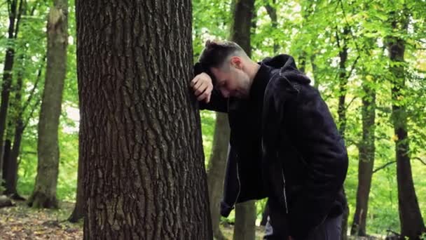 深いうつ病のために泣いて 彼の頭を保持する森の中の木の近くに立っている悲しいストレスの男性の顔 顔の表情を怒らせたトラブルの問題を心配 — ストック動画