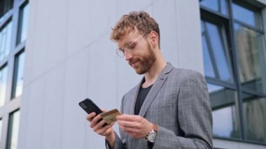 Banka kartı tutan mutlu iş adamı, cep telefonu internet alışveriş uygulamasına CVV kodu ya da ödeme bilgisini girerken, mal satın alma ya da e-bankacılık hizmetlerini çevrimiçi olarak görünce şaşırıyor