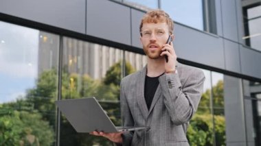 Bilgisayarlı ve gözlüklü genç iş adamı cep telefonuyla konuşuyor. Aramalara cevap veriyor. Ofis uzaktaki görüşme pazarlığının yakınındaki detaylı bilgi için bilgisayar ekranına bakıyor.