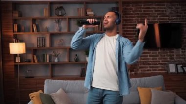 Neşeli Eğlenceli Afro-Amerikan Genç Adam Salonda Dans Ediyor, Çekici mutlu adam eğleniyor Boş zamanını TV kumandasına şarkı söyleyerek geçiriyor, evde müzik dinliyor