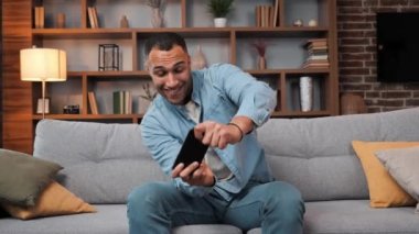 Neşeli Afrikalı Amerikalı adam akıllı telefonda video oyunu oynamaktan zevk alıyor. Eğleniyor, dinleniyor, kanepede oturuyor. Modern grafikler ve eğlenceli oyunlarla güzel bir oyun. İnsanlar ve aletler kavramı