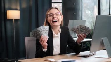Heyecanlı iş kadını para gösteriyor. Ofiste dolar banknotları var. Başarının, kazancının, zaferin sembolü. Zengin kadın, insan kavramına ulaş. Zeki kadın gülümsüyor, çok para kazanıyor.