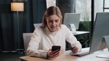 Happy millennial pretty woman holding bank card winning lottery, got amazing news, entering cvv code or payment information in mobile internet shopping application, feeling amazed of purchasing goods