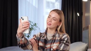 Energetic happy pretty blonde girl smiling face waving hand talking on mobile video call make videoconference at home talking chatting by virtual video app online videocall meeting Blogger influencer