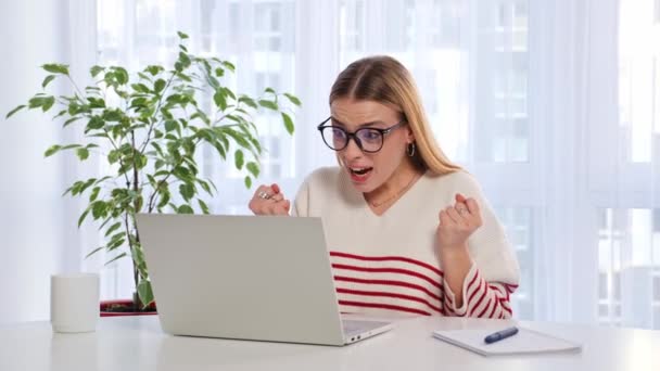 眼鏡で喜びの少女学生は成功を祝うオンラインノートパソコンを使用して素晴らしいニュースを読む家に座って驚いた感じ 幸せな興奮した女性は良いテスト結果奨学金を得ました — ストック動画
