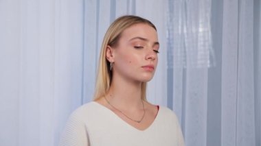 Close up view of serious woman looking to camera. Portrait of confident girl in a white sweatshirt turning head folding hands. Beautiful attractive lady with beautiful hair, people and emotions