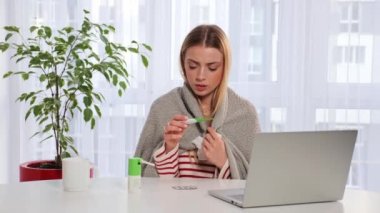 Sick Businesswoman Wrapped in Blanket Using Thermometer Test For Flu, Cold And Body Temperature Makes Inhalations for the Throat, Cough Spray While Working With Laptop In The Living Room At Home