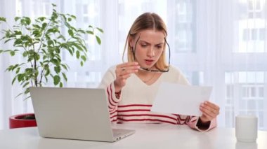 Sad shocked woman girl sitting on couch at home reads received bad news holds documents paper letter feels desperate about eviction not passing the exam, domestic bills or debt, college expulsion