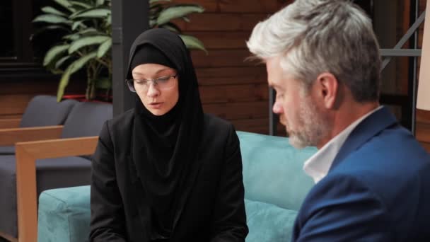 現代のオフィスで商業オファーの論文を提示契約の詳細を説明する男性パートナーとの交渉を持つ深刻なビジネスイスラム教徒のアラビア人女性 会社の国際代表 — ストック動画
