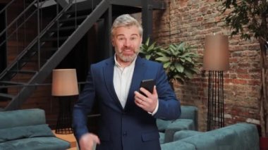 Happy Excited overjoyed business man using mobile phone app in modern loft office. Positive businessman looking at mobile phone with emotion winner or win, financial stock sports betting game