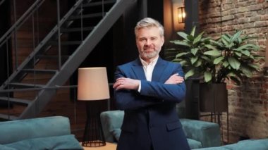 Portrait of confident berded middle age businessman turning head to camera and smiling while crossing arms proud entrepreneur enjoying successful startup company in a modern loft meeting room