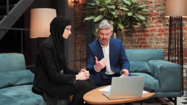 Two multicultural businessmen discuss the project, commercial offer in a meeting room. A sales manager holding a document with an investment project tells a Muslim investor about favorable conditions