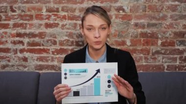 Serious businesswoman talking to camera making online conference business call, explains the data of graph, increase in profit due to additional investments. Confident teacher, distance interview. 