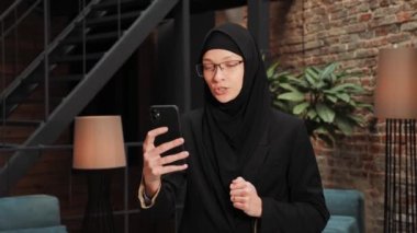 Cute beautiful young arabic businesswoman using modern smartphone, passing online job interview, distant communication. Confident business woman talk to webcam make video conference call in office