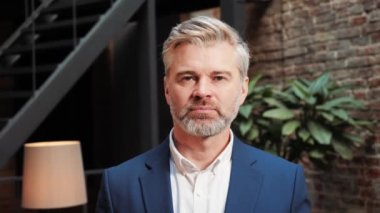 Confident focused businessman wearing classic suit looking at camera in office, concentrated male employee executive face satisfied with good job career posing in modern office, close up man portrait