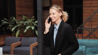 Happy millennial professional investor banker businesswoman stand in modern office talk on phone, smiling young entrepreneur speak on cellphone, mobile tech conversation online communication concept