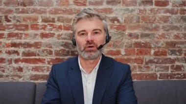 Arkadaş canlısı orta yaşlı çekici pazarlamacı temsilcisi web kameralı dizüstü bilgisayarla konuşuyor. İş adamı kulaklık takıyor ve video konferans çağrısı yapıyor. Çağrı merkezinde müşteri destek servisi