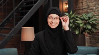 Siyah geleneksel tesettürlü güzel bir Arap kadının portresi doğrudan kameraya bakıyor ve modern çatı katında gülümsüyor. Gülümseyen güzel bir kadın yüzü. Arap başörtüsü