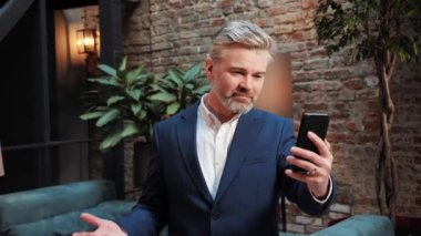 Başarılı bir iş adamı bankacı danışmanı cep telefonunu kullanarak konferans salonunda video görüşmesi yapıyor. Erkek yatırımcı, akıllı telefon teknolojisiyle çevrimiçi sohbet ediyor.