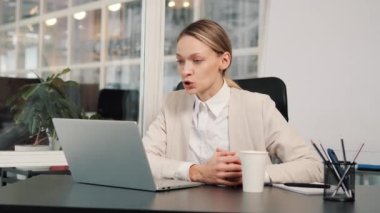 Serious business woman talking on video conference online in office. Pretty worker having video call on laptop computer indoor. Female professional explaining project talking to web cam at workplace