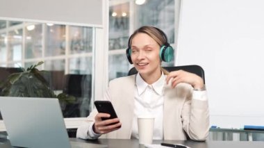 Kulaklıklı mutlu genç bir kadın cep telefonuyla şarkı söylüyor ve yüksek sesli müzik dinliyor. Ofis masasında dizüstü bilgisayarla oturuyor. Tembel işçi iş yerinde iş yerinde vakit harcıyor.