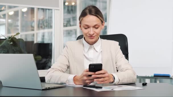 職場で携帯電話のタップメッセージを使用して幸せなビジネス女性を閉じます オフィスのスマートフォンでインターネットを閲覧する笑顔の女性 携帯電話でメッセージを読むビジネス女性の肖像 — ストック動画