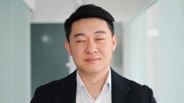Close up chinese face portrait. Handsome smiling asian business man in formal suit looks at camera in office hallway. East Asian male businessman working on financial, marketing, banking projects