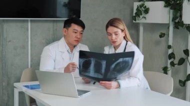 İki farklı doktor konuşur ve kullanır, dizüstü bilgisayar kullanır, hastanın röntgenini analiz eder, Analiz Sağlık Kliniği, Asyalı baş cerrah ve radyoloji uzmanı hastaların akciğerlerinin görüntüsü hakkında fikir alışverişinde bulunur.