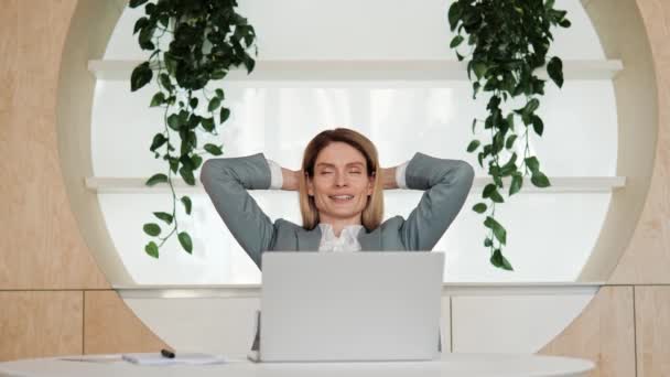 成功した笑顔の満足した若いビジネス女性は職場の机に座ってストレッチ仕事を終えた 仕事が終わった後ストレス解消を感じる幸せなリラックスしたビジネスマン頭の後ろに手を置く — ストック動画