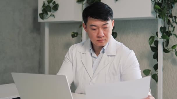Fókuszált Férfi Ázsiai Háziorvos Fehér Egyenruhában Munkahelyén Papírmunkát Végez Laptopot — Stock videók