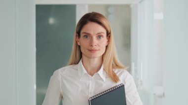 Confident dreaming young successful business woman agent office worker deep in thoughts look to camera in hallway, happy female human face friendly businesswoman holding folder smile close up