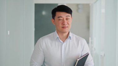 Successful Asian Businessman with Folder Looking Smiling to Camera, Standing in Modern Glass Bright Office Hall, Working on Financial, Business and Marketing Projects. Portrait of Korean Manager