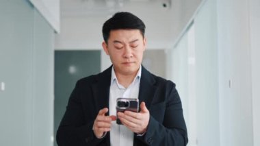 Genç sinirli sinirli sinirli Asyalı iş adamı ofis salonunda cep telefonu kullanıyor. Veri girilemiyor, zayıf internet ağı yok, hata. Erkek kullanıcı kötü haber ya da kayıp sinyal yüzünden hayal kırıklığına uğradı