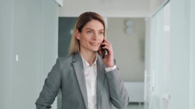 Cheerful beautiful blue eyes businesswoman making mobile call in office hall. Office manager talking on smartphone consulting bank client remotely. Successful adviser discussing project with partner
